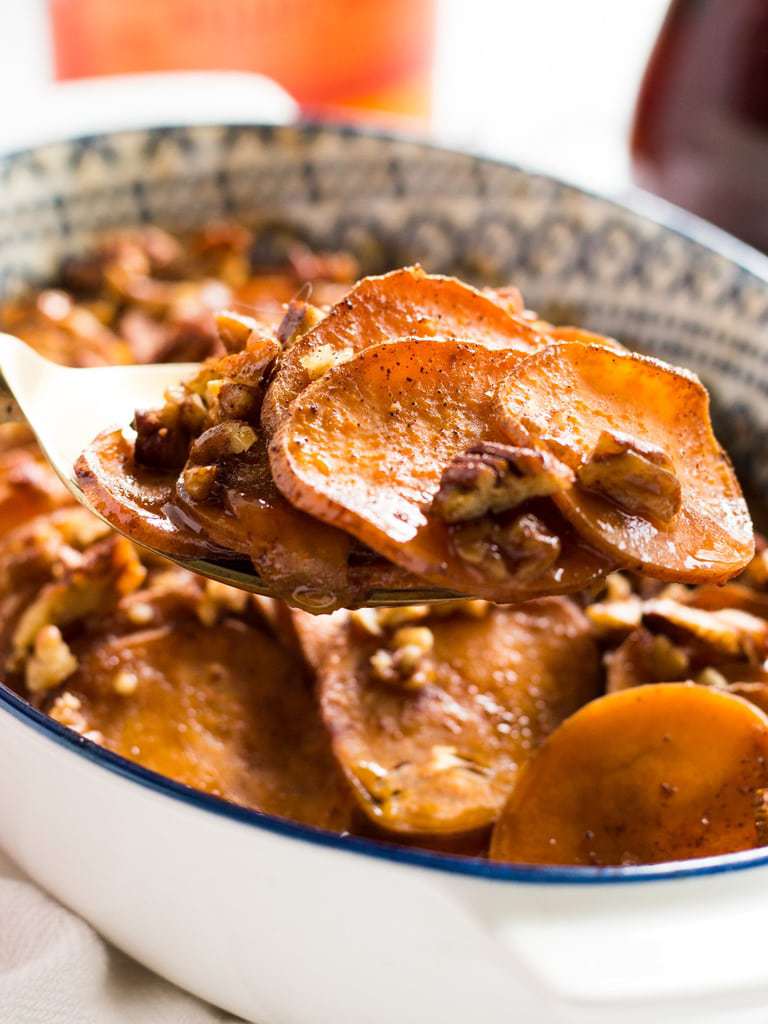 serving spoon holding sweet potato rounds with pecans and glaze in a casserole dish.