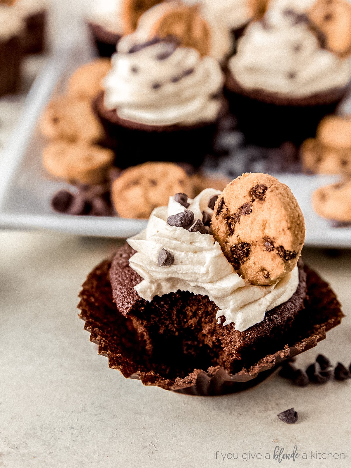 Chocolate chip cookie dough frosting cupcake on unwrapped cupcake liner and bite taken from the cupcake