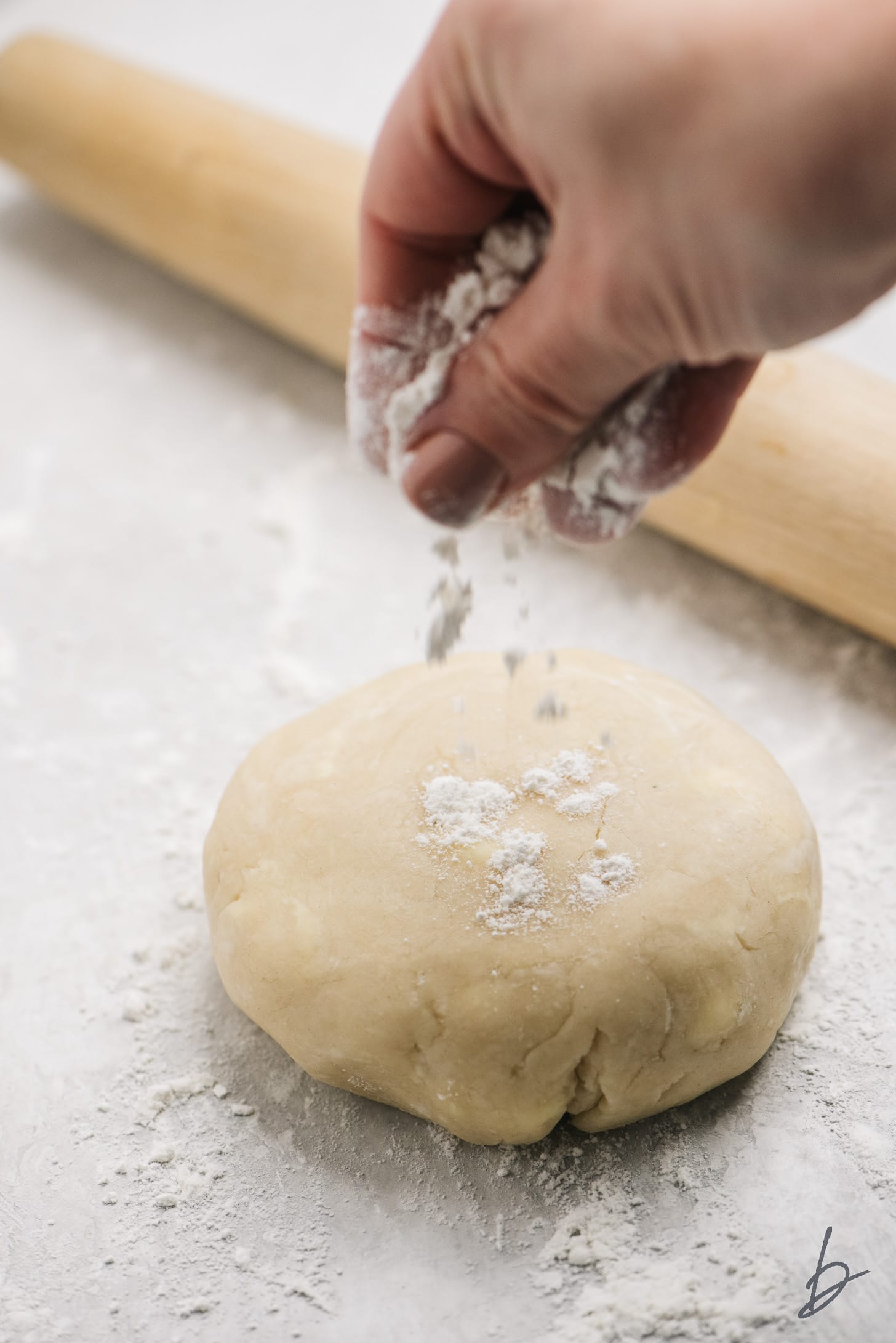 hand dusting flour on top of ball of chilled pie crust dough.