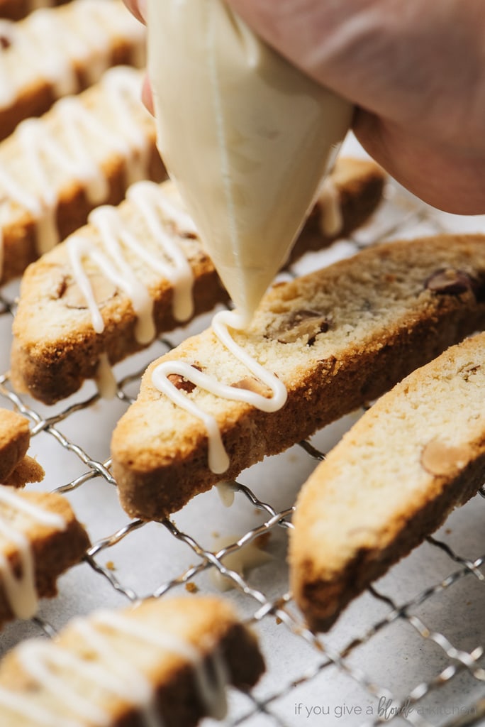 icing bag drizzling icing on almond biscotti
