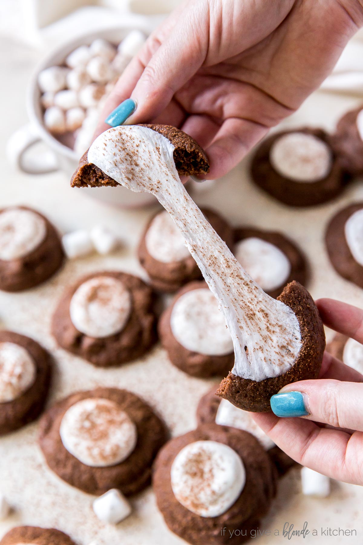 hands pulling hot cocoa cookie apart to show gooey marshmallow