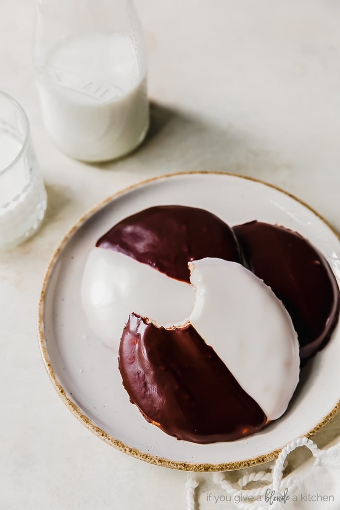 plate of three black and white cookies; top cookie has a bite taken out of it