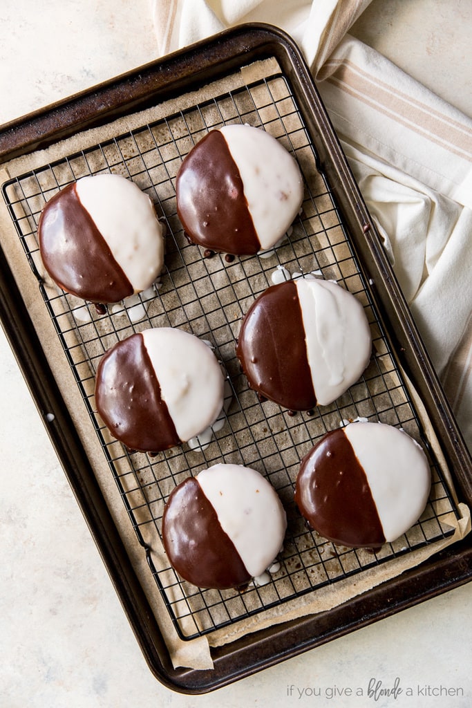 six black and white cookies on wire rack on parchment paper