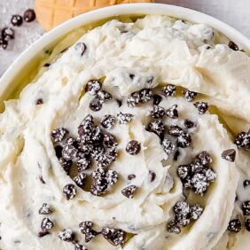 cannoli dip in bowl topped with mini chocolate chips and dusting of confectioners' sugar