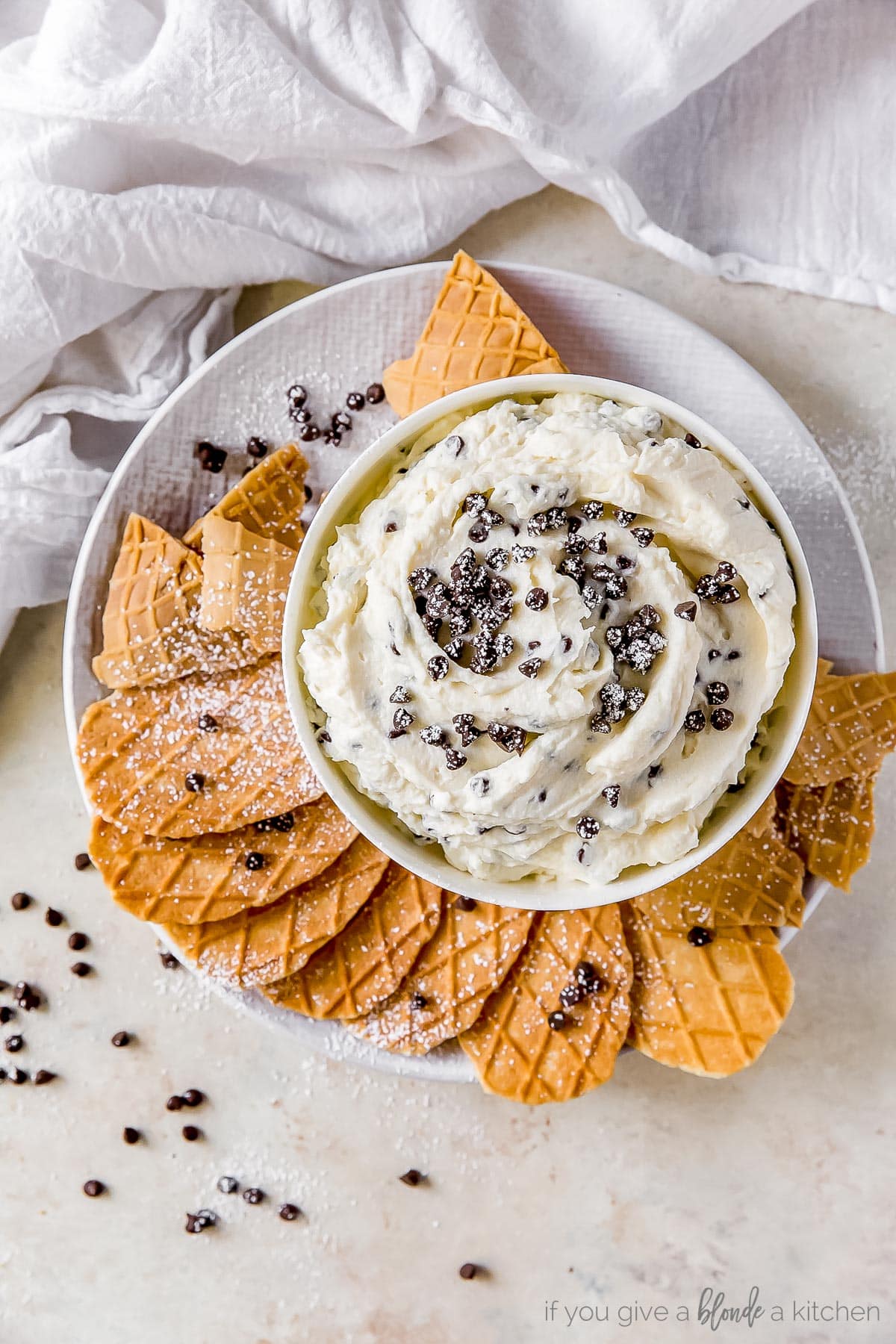 cannoli dip with mini chocolate chips in a bowl on plate with pizzelle cookies