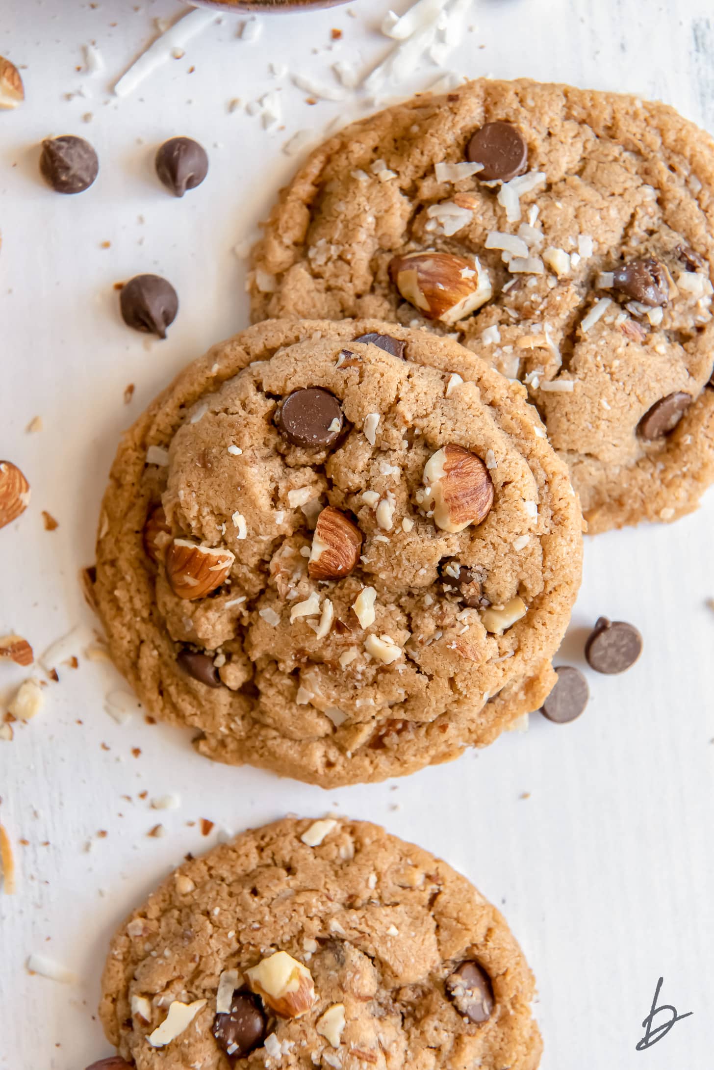 almond butter cookie resting on another cookie, both with chocolate chips, shredded coconut and almond pieces.