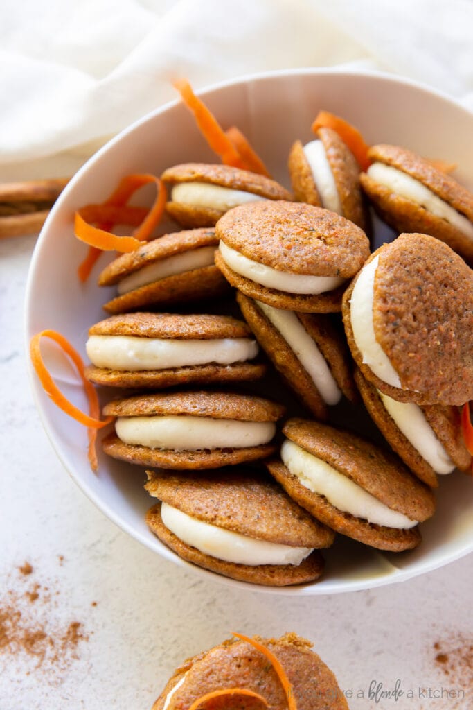 bowl filled with carrot cake whoopie pies and a couple pieces of shredded carrots