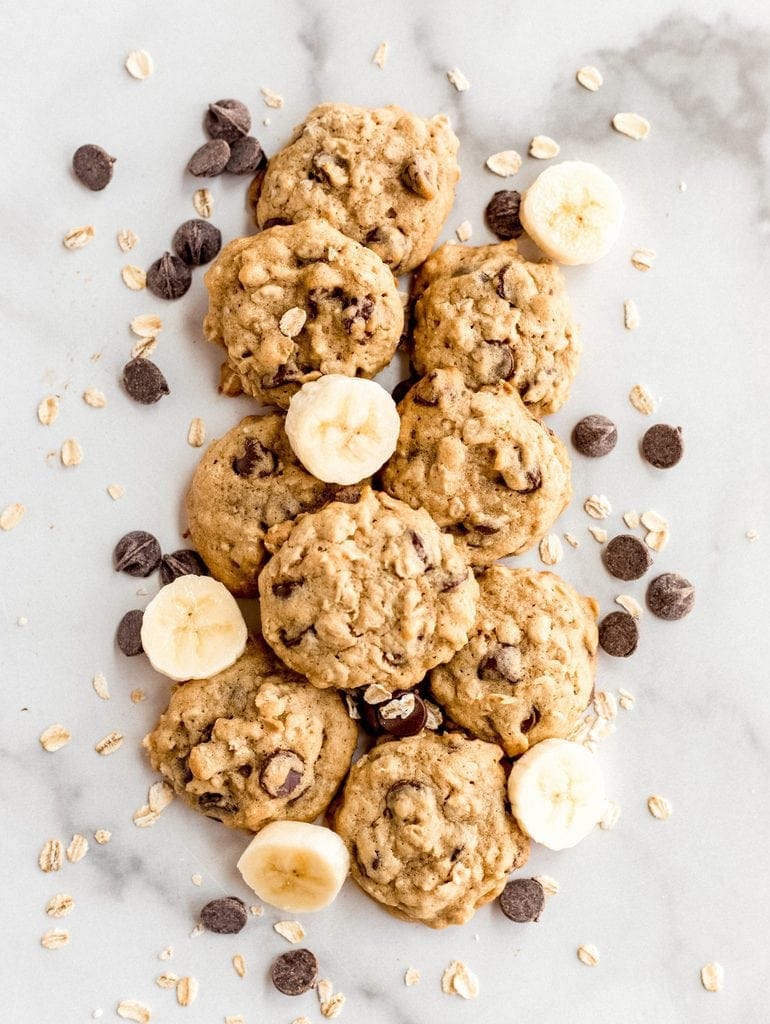 banana oatmeal cookies on marble with slices of banana, chocolate chips and oats