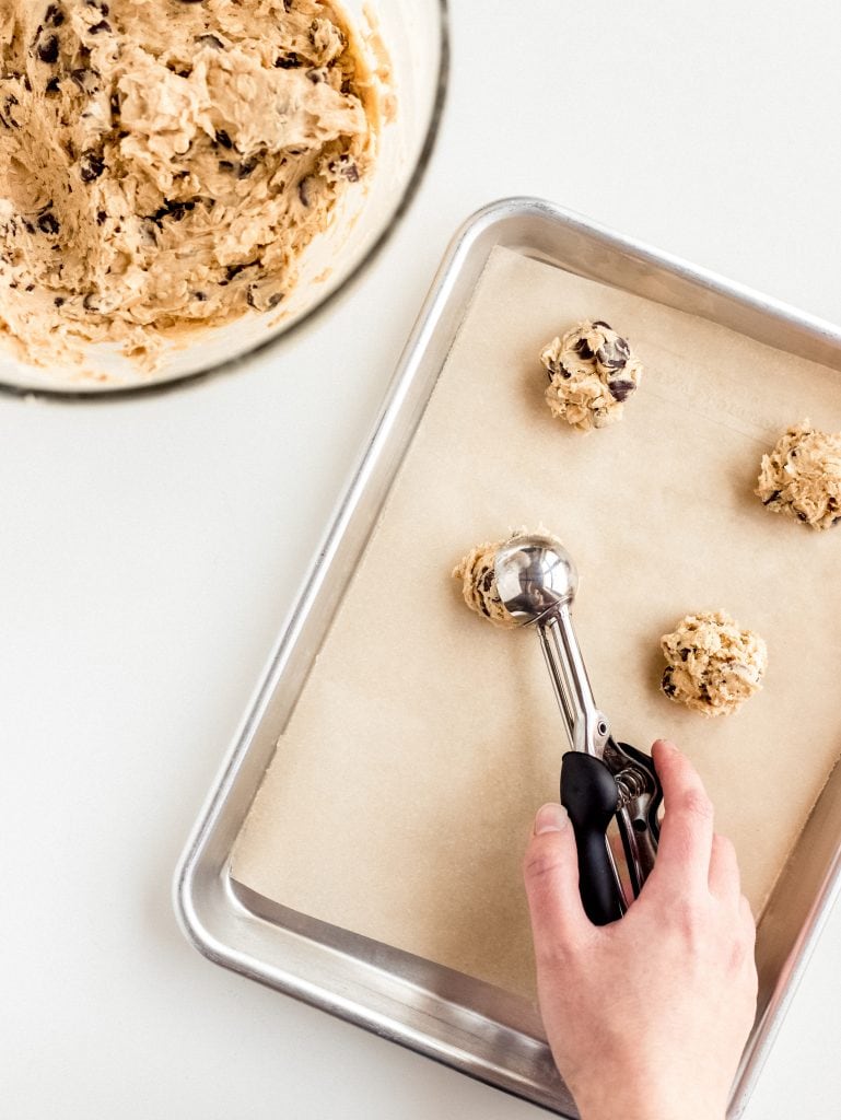 hand scooping cookie dough onto parchment lined baking sheet