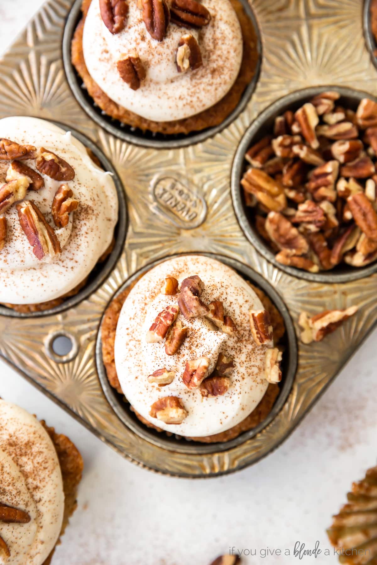 antique muffin tin with hummingbird cupcakes topped with cream cheese frosting and pecans