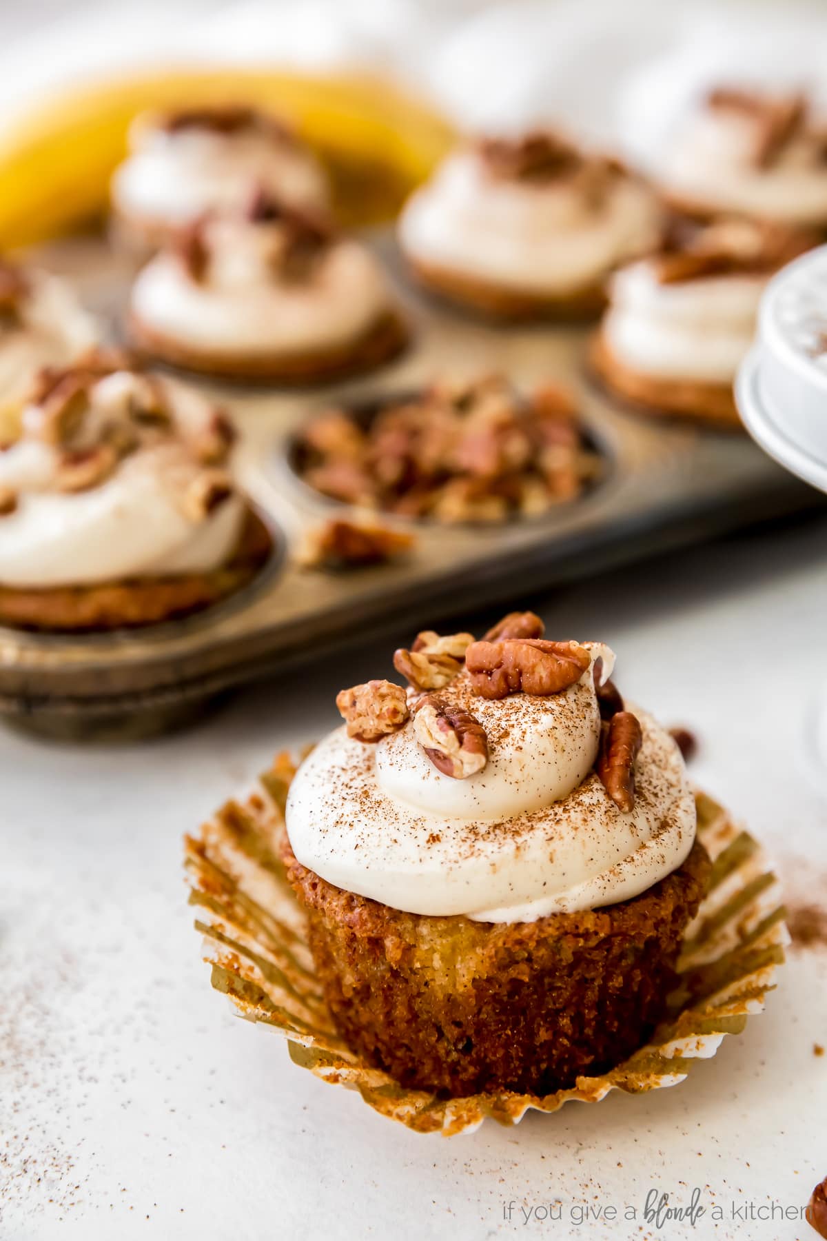 hummingbird cupcake on open paper muffin liner with tin of cupcakes behind it