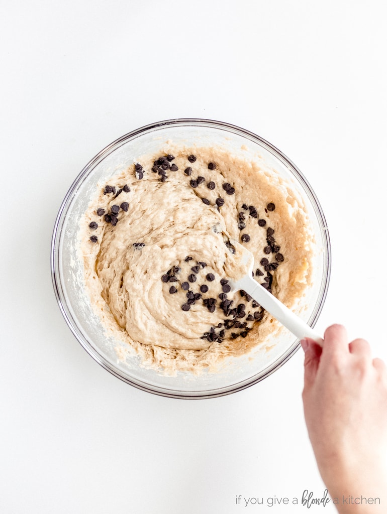 hand stirring spatula mixing chocolate chips into banana muffin batter