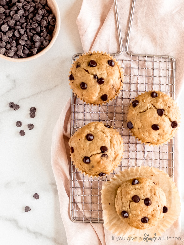 banana chocolate chip muffins on cooling rack and pink kitchen towel bowl of chocolate chips