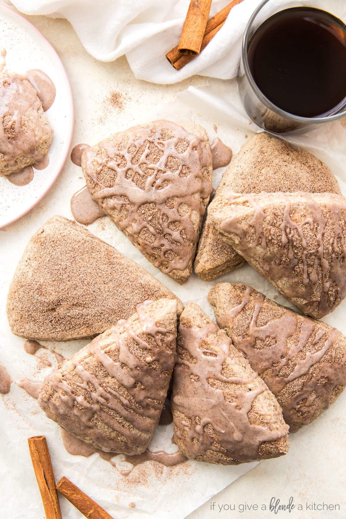 cinnamon scones topped with cinnamon glaze in a circle on parchment paper next to glass of coffee