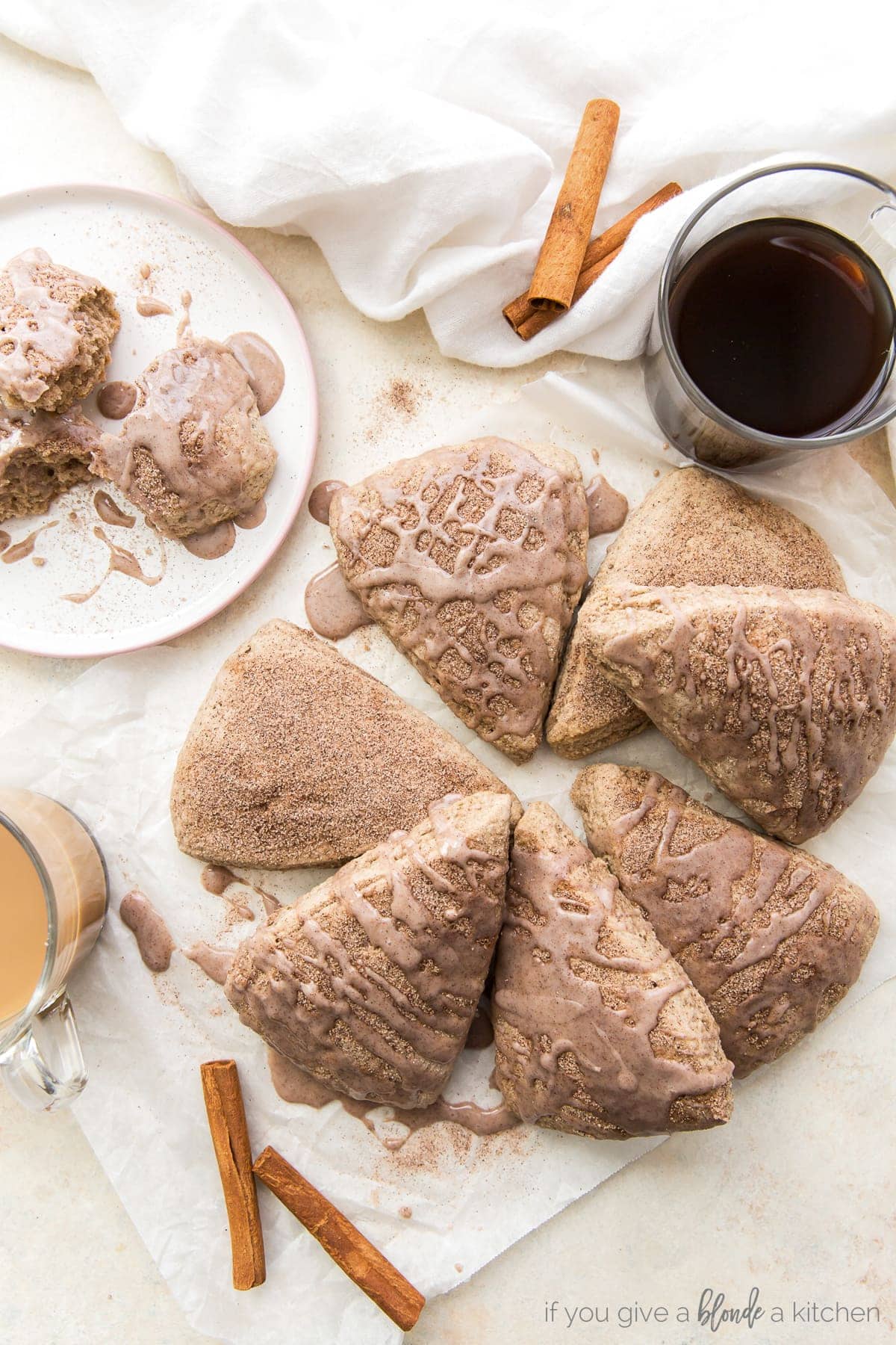 cinnamon scones topped with cinnamon glaze in a pile on parchment paper next to cinnamon sticks