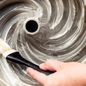 hand holding pastry brush spreading cake pan release mixture inside bundt cake pan