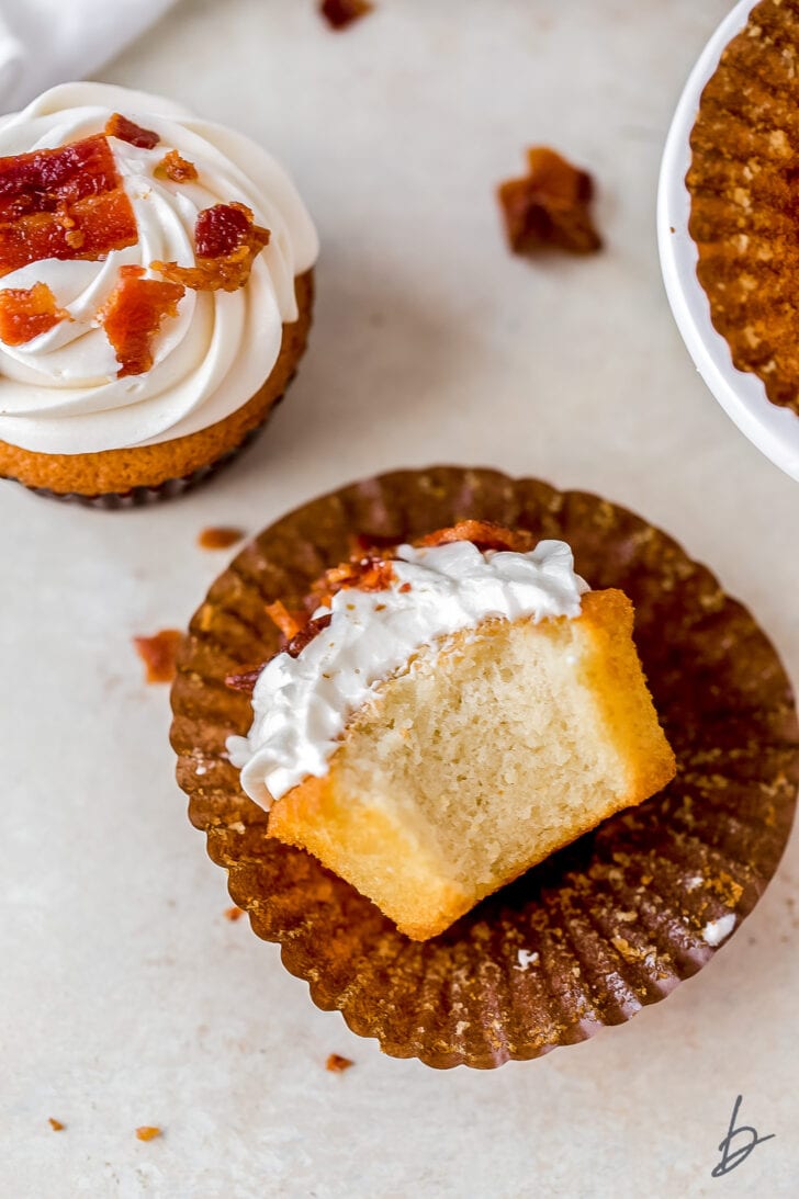 maple bourbon cupcake with a bite taken out of it lying on its side on brown paper cupcake liner