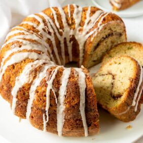 cinnamon zucchini bundt cake with glaze dripping down and two slices cut out