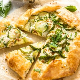 zucchini galette on parchment paper with two slice cut away near basil leaves
