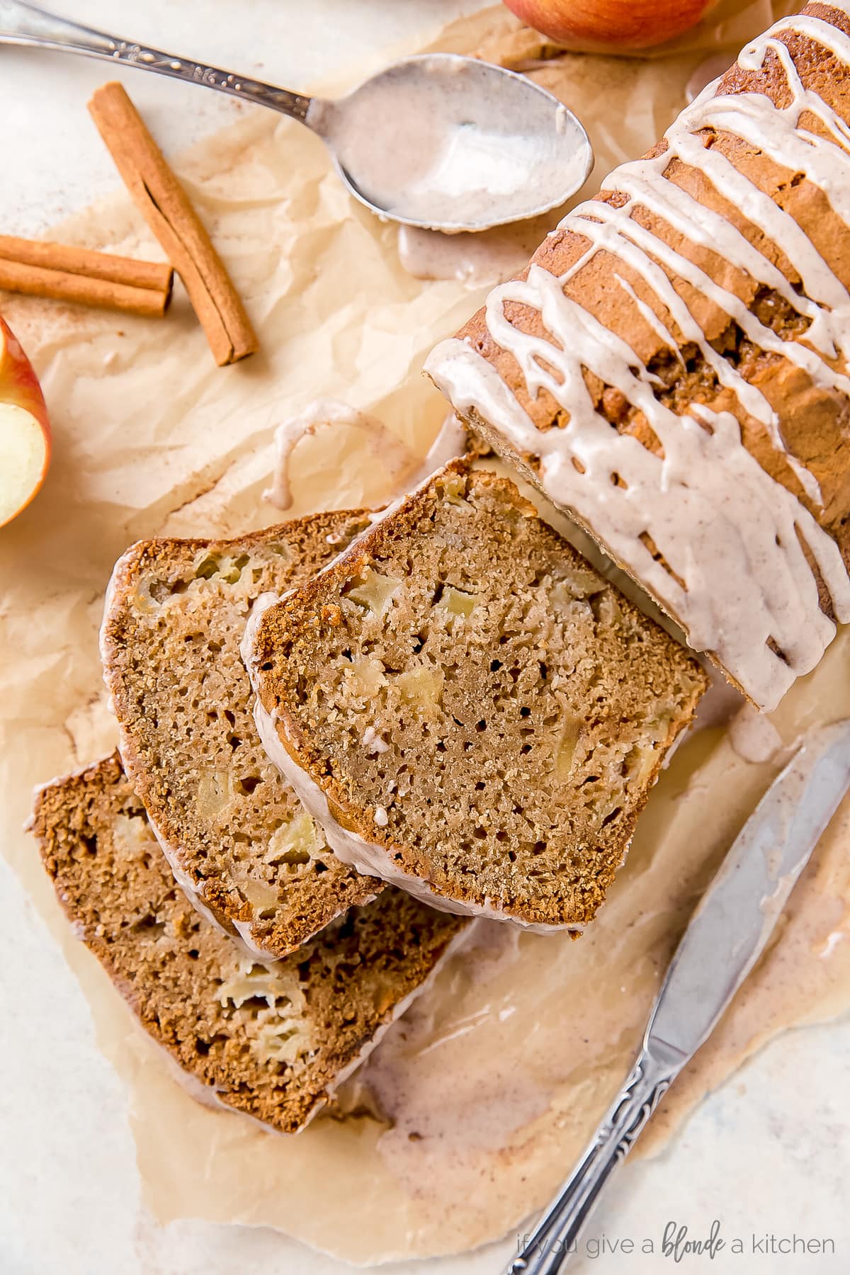 loaf of apple cider bread with glaze and three slices on top of parchment paper