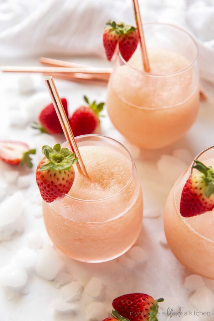 frose in stemless wine glasses with metal straws and strawberries on the rim