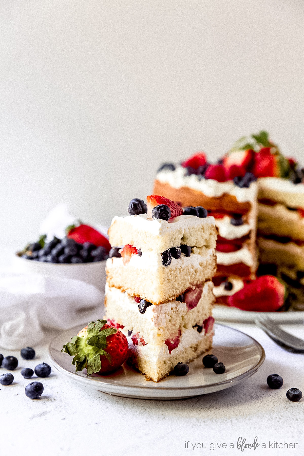 slice of triple berry layer cake on plate with strawberry and blueberries