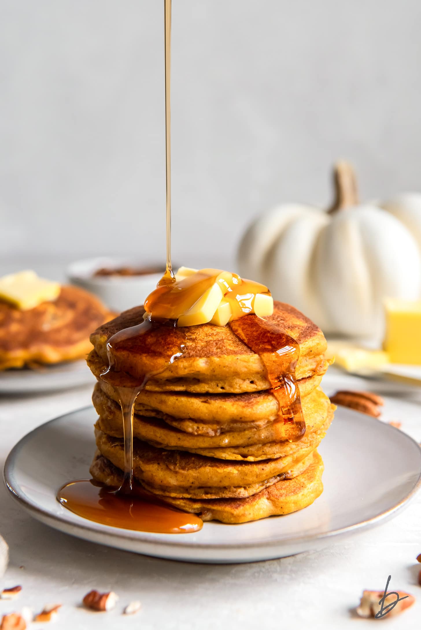 maple syrup poured on stack of fluffy pumpkin pancakes.
