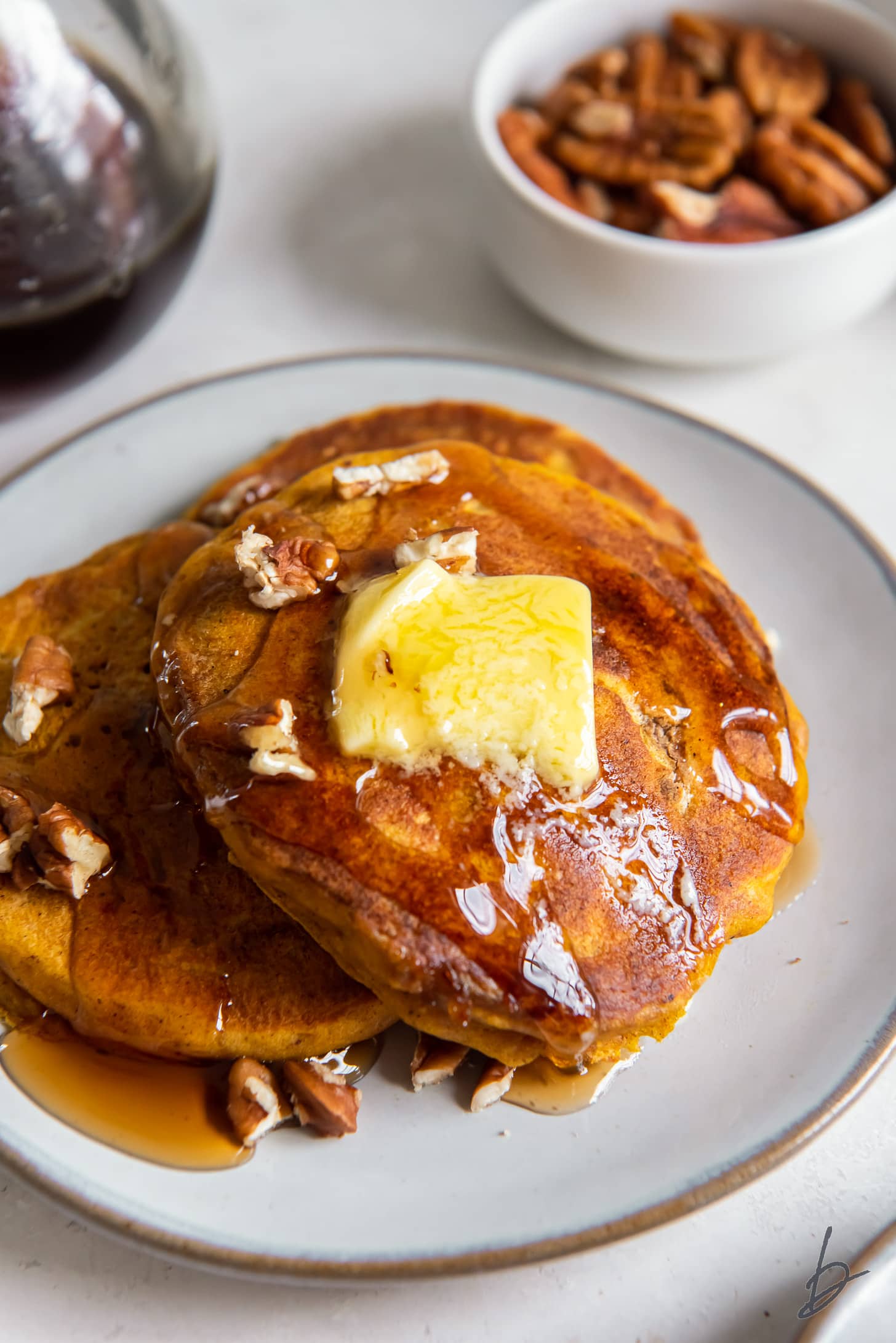 two pumpkin pancakes topped with maple syrup, butter and pecans on gray plate.