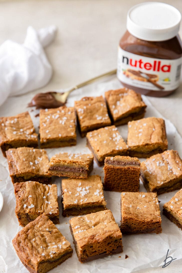 salted nutella blondies on crinkled wax paper and jar of nutella behind bars