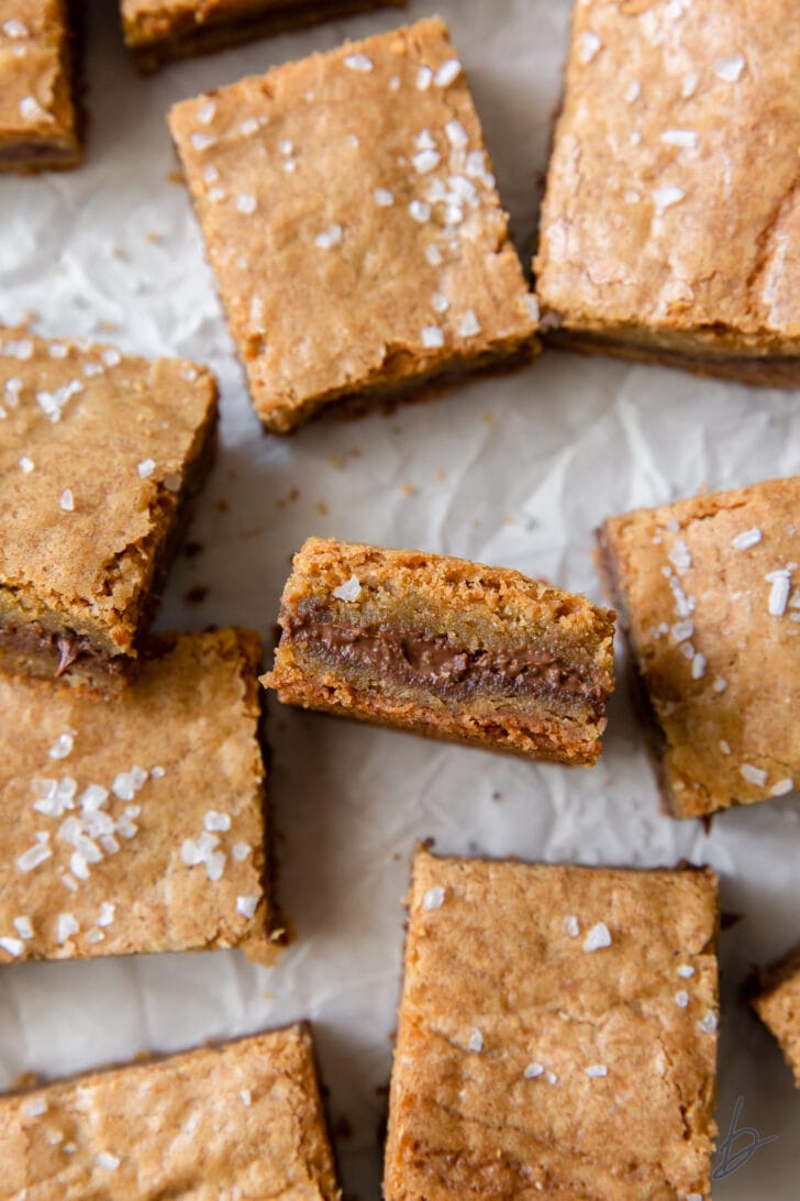 salted nutella blondies on crinkled wax paper with one blondie on its side to show nutella inside