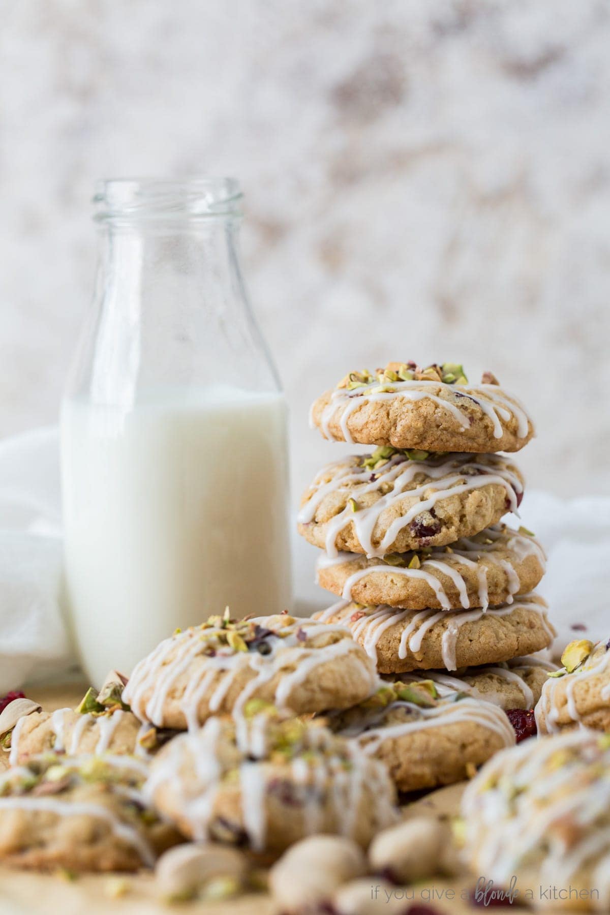 pile of cranberry pistachio oatmeal cookies with icing next to bottle of milk