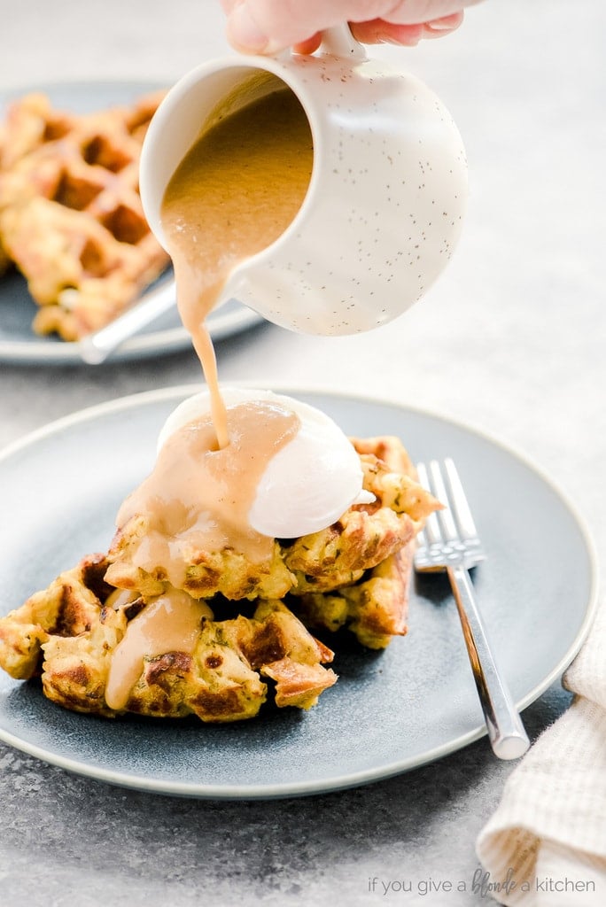 hand pouring gravy over poached egg and stuffing waffles