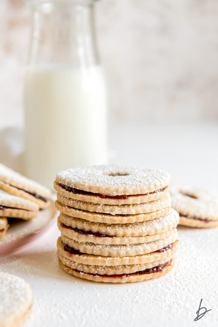 Stack of linzer cookies with raspberry jam with glass bottle of milk behind cookies