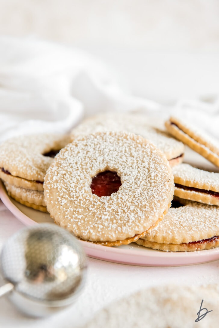 linzer cookie sandwich dusted with confectioners sugar and top cookie with circle hole showing raspberry jam inside
