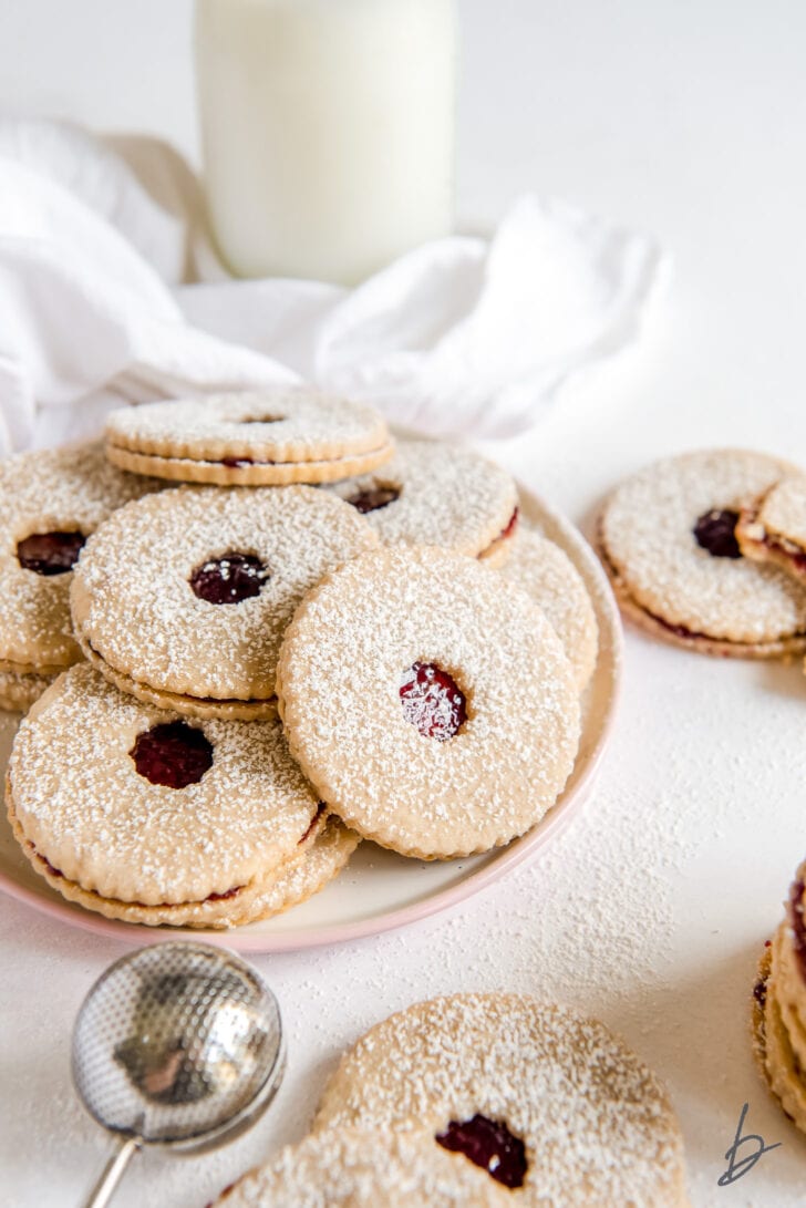 linzer cookies in a pile on plate with glass milk bottle behind plate