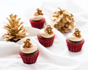 mini gingerbread cupcakes in red cupcake liners with gingerbread man candy on top