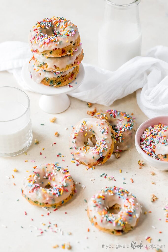 birthday donuts with icing and sprinkles on surface with glass of milk and sprinkles
