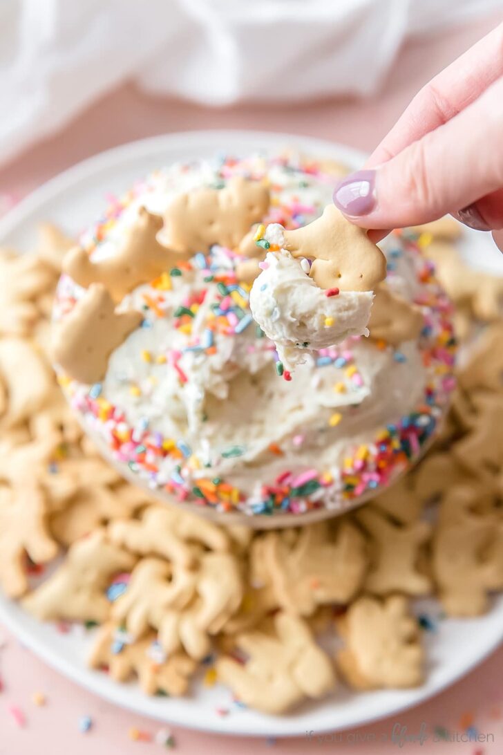 hand dipping animal cracker in funfetti dip