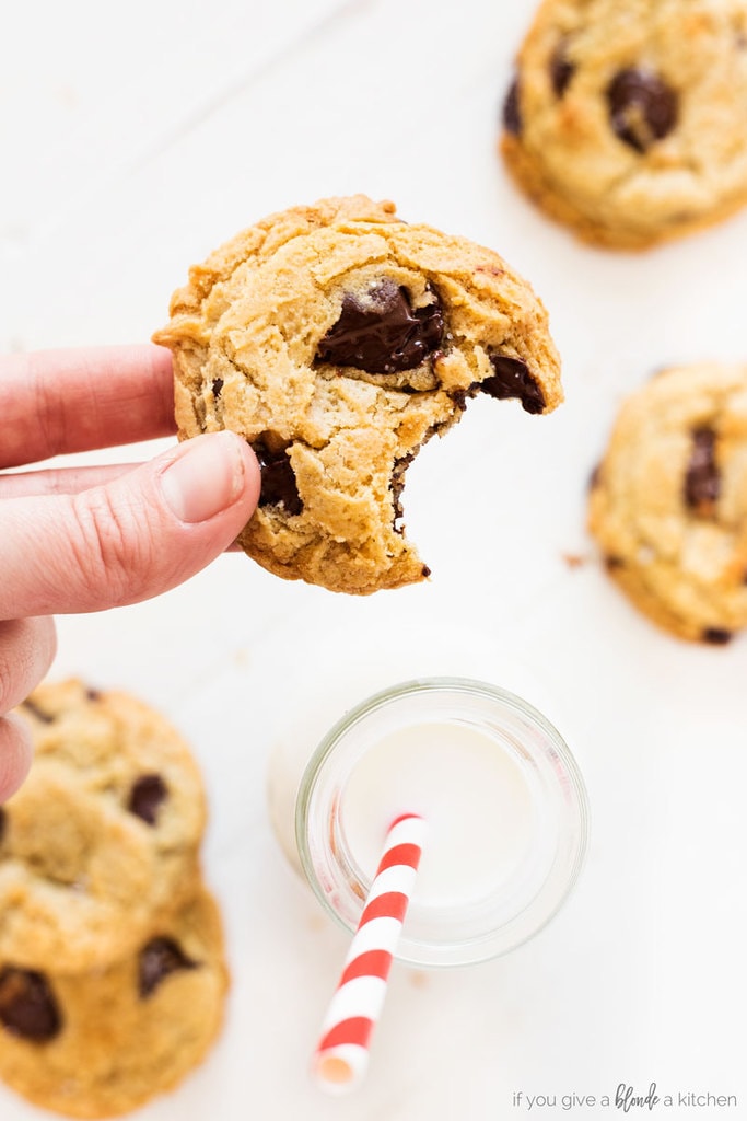 homemade chocolate chip cookies with bite and brown sugar stacked next to a glass bottle of milk