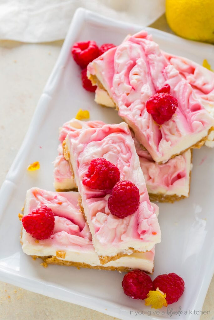 no bake raspberry cheesecake bars stacked on white plate with fresh raspberries