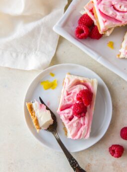 raspberry cheesecake bar on white plate with fresh raspberries and fork taking a piece