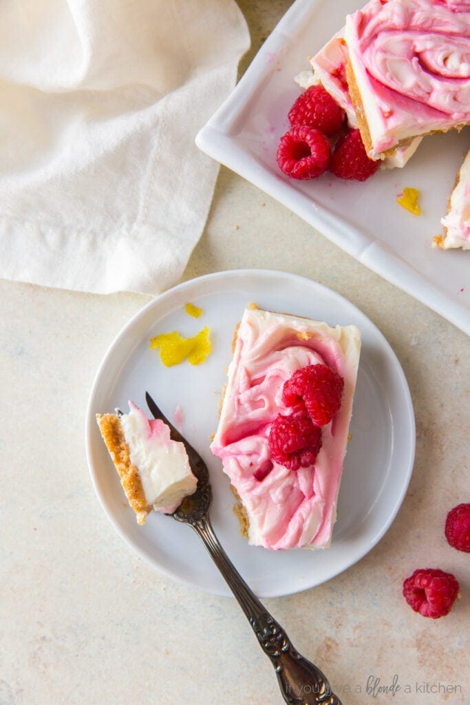 raspberry cheesecake bar on white plate with fresh raspberries and fork taking a piece