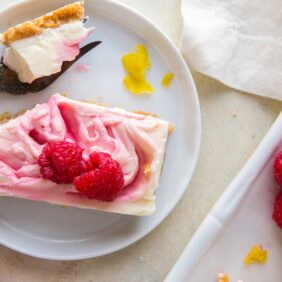 raspberry cheesecake bar with fork taking a bite on round white plate with lemon zest