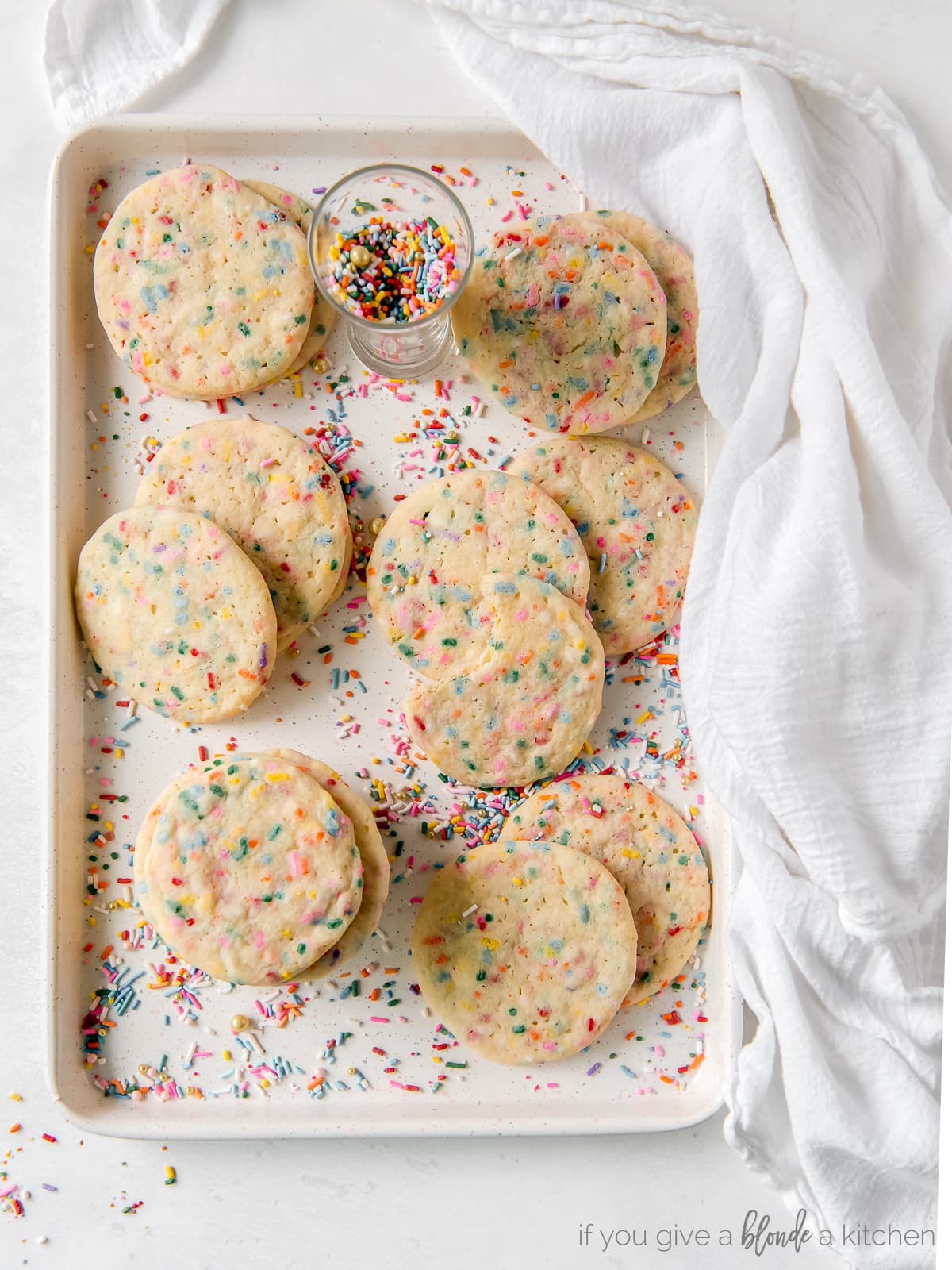 white cloth wrapped around baking sheet with sprinkle sugar cookies and rainbow sprinkles