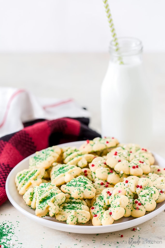 spritz cookies with sprinkles on white round plate; milk bottle with straw behind plate