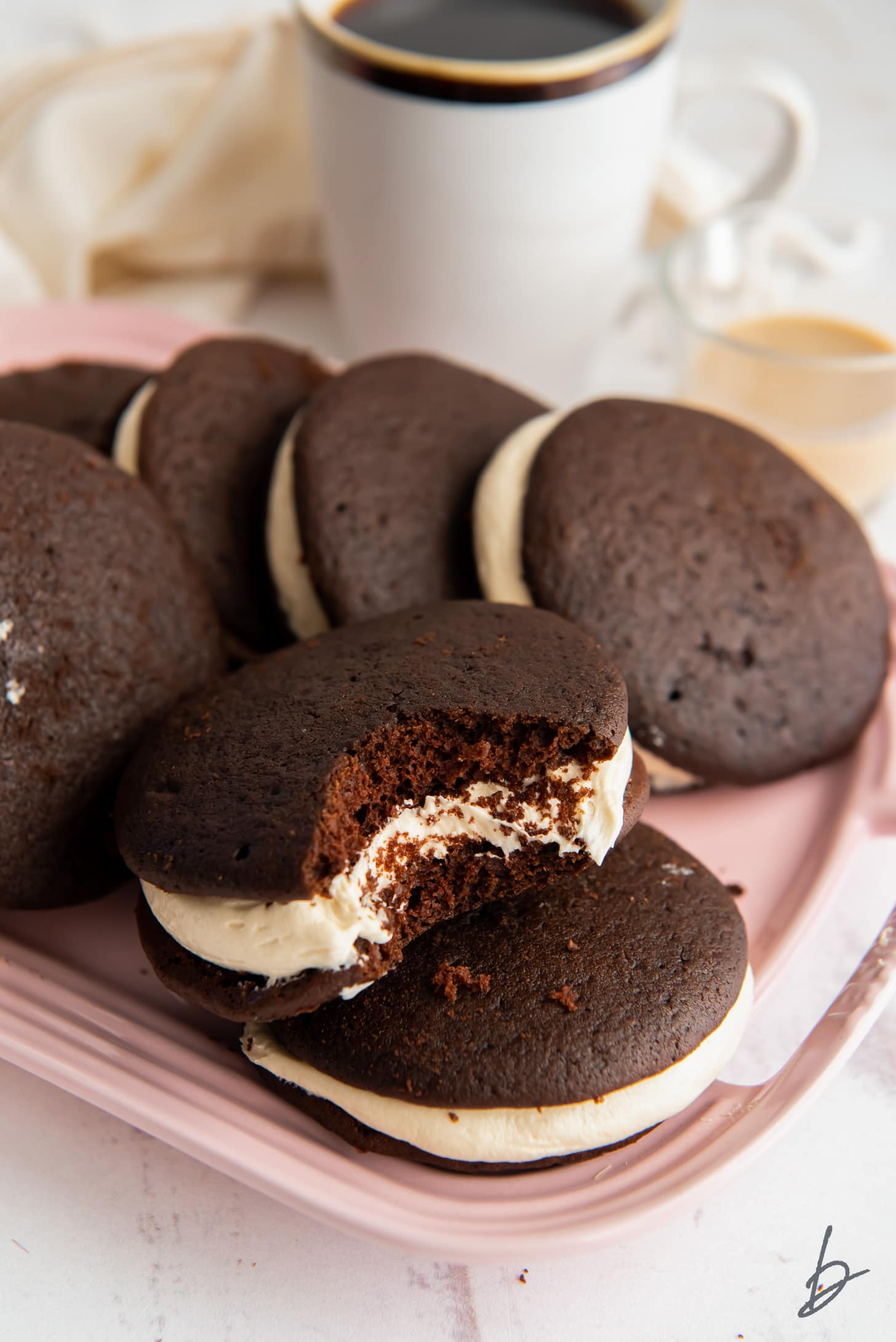 pink plate of chocolate whoopie pies with baileys buttercream frosting and one whoopie pie with a bite taken out of it