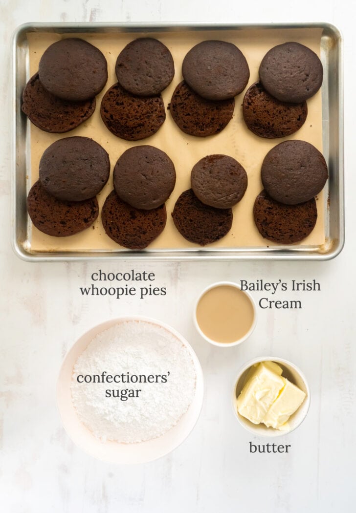 baileys frosting ingredients in bowls labeled with text next to sheet pan of baked chocolate whoopie pies