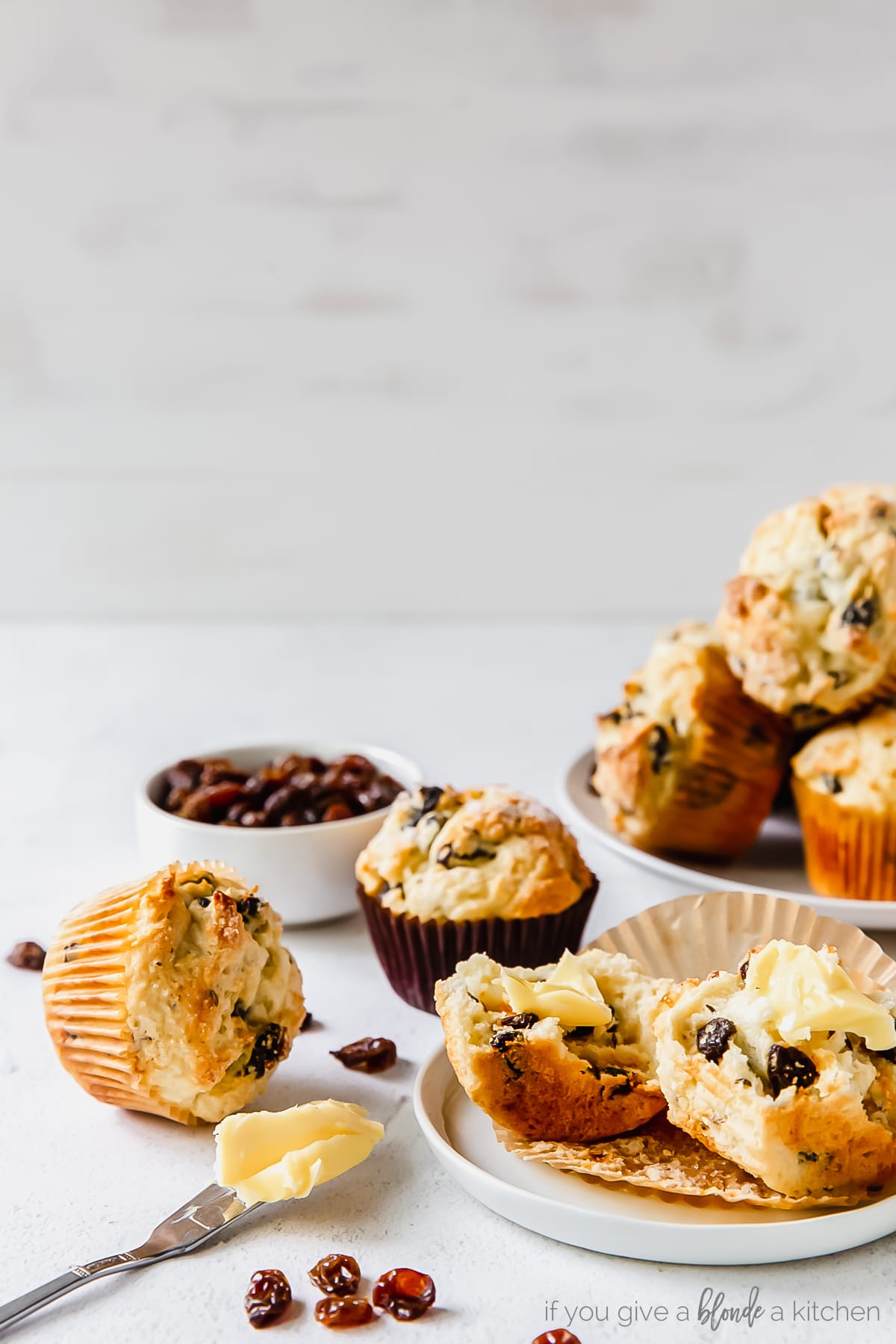 irish soda bread muffin cut in half with butter on knife next to more muffins and raisins.