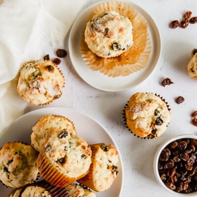 Irish soda bread muffins piled on a plate with one muffin on a smaller plate and bowl of raisins