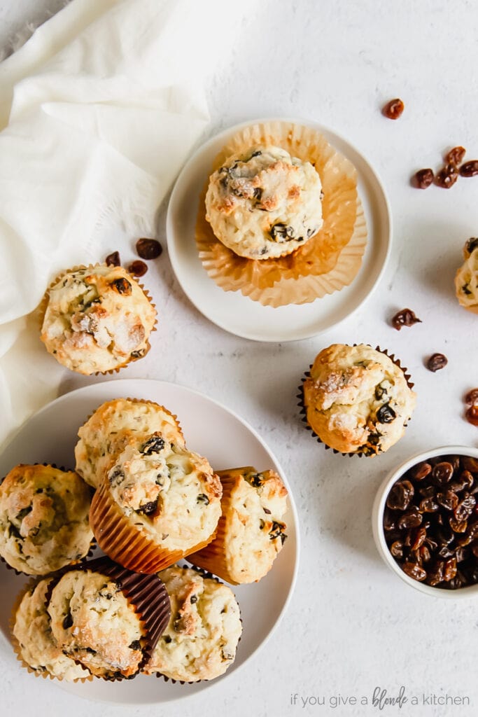Irish soda bread muffins piled on a plate with one muffin on a smaller plate and bowl of raisins